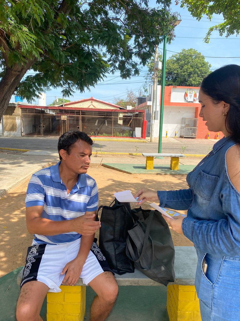 man wearing a black jacket, white shirt, blue jeans, and brown boots, playing a white electric guitar while sitting on an amp